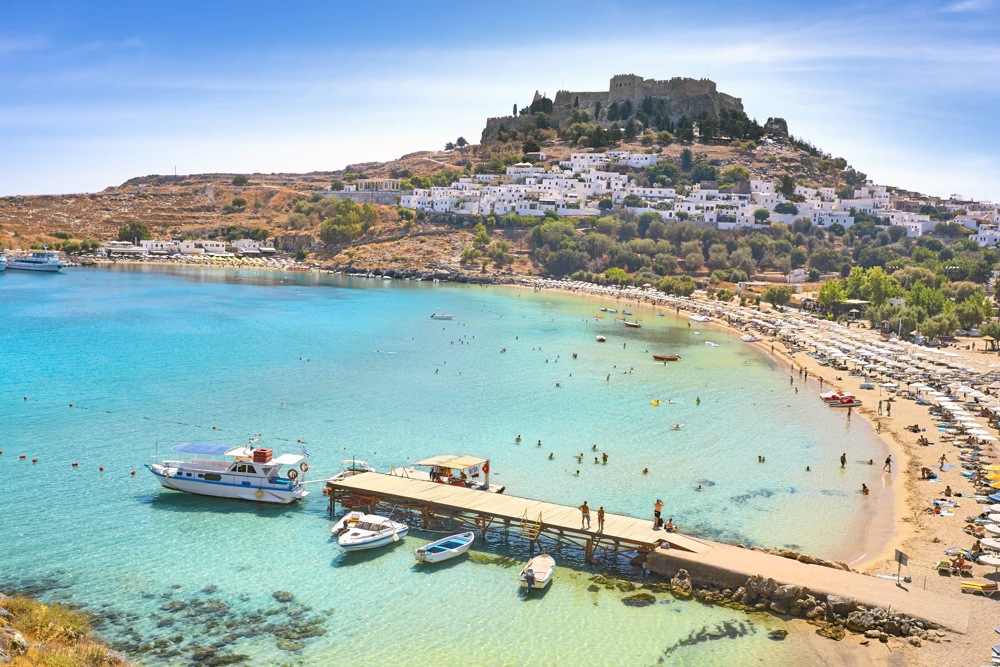 St. Paul's Bay, Rhodes Island, Greece: a beach with turquoise water, boats, and a hilltop castle.