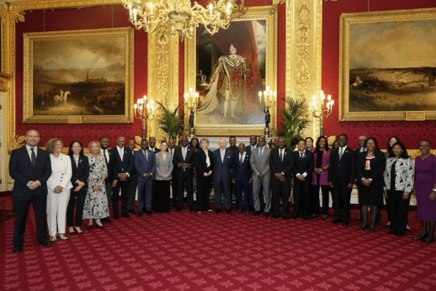 King Charles standing with Caribbean officials in a grand room beneath a controversial portrait of King George IV.