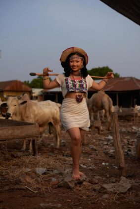 Pearl Shim Mugalla posing in traditional Fulani attire with a camel in a dusty Sahel landscape