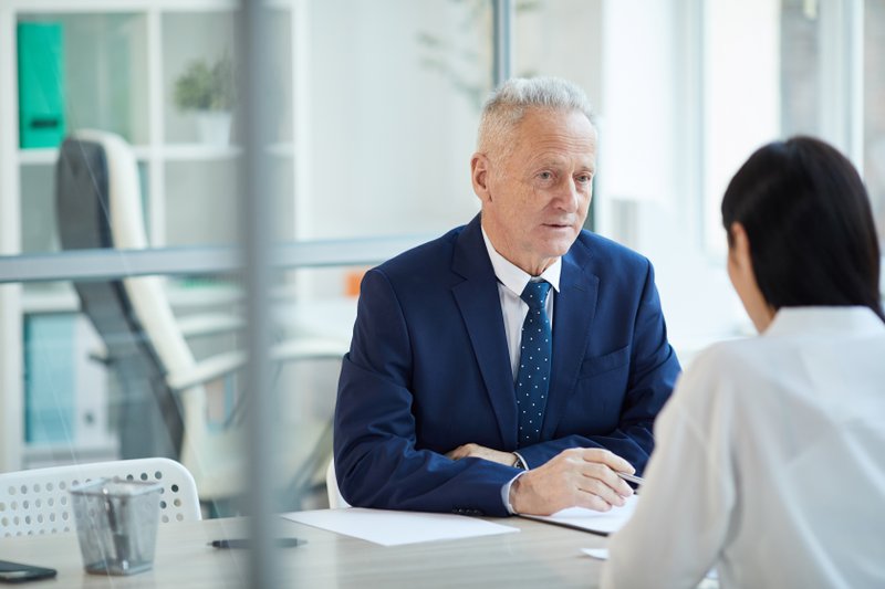 Portrait of successful senior businessman interviewing young woman for job position in office, copy space