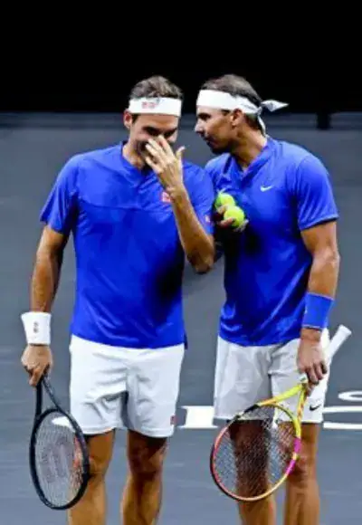 Roger Federer and Rafael Nadal are laughing together on a tennis court, holding rackets and balls, in a moment you can watch via BYiPTVSHOP.