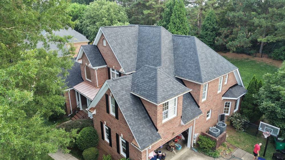 Drone view of a red-brick two-story home with a new charcoal shingle roof