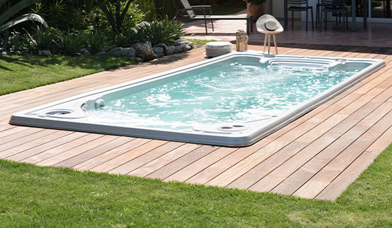 Spa de nage encastré dans une terrasse en bois avec du gazon autour