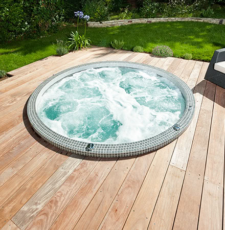 Spas gamme mosaïque encastré dans une terrasse en bois avec des plantes dans le fond