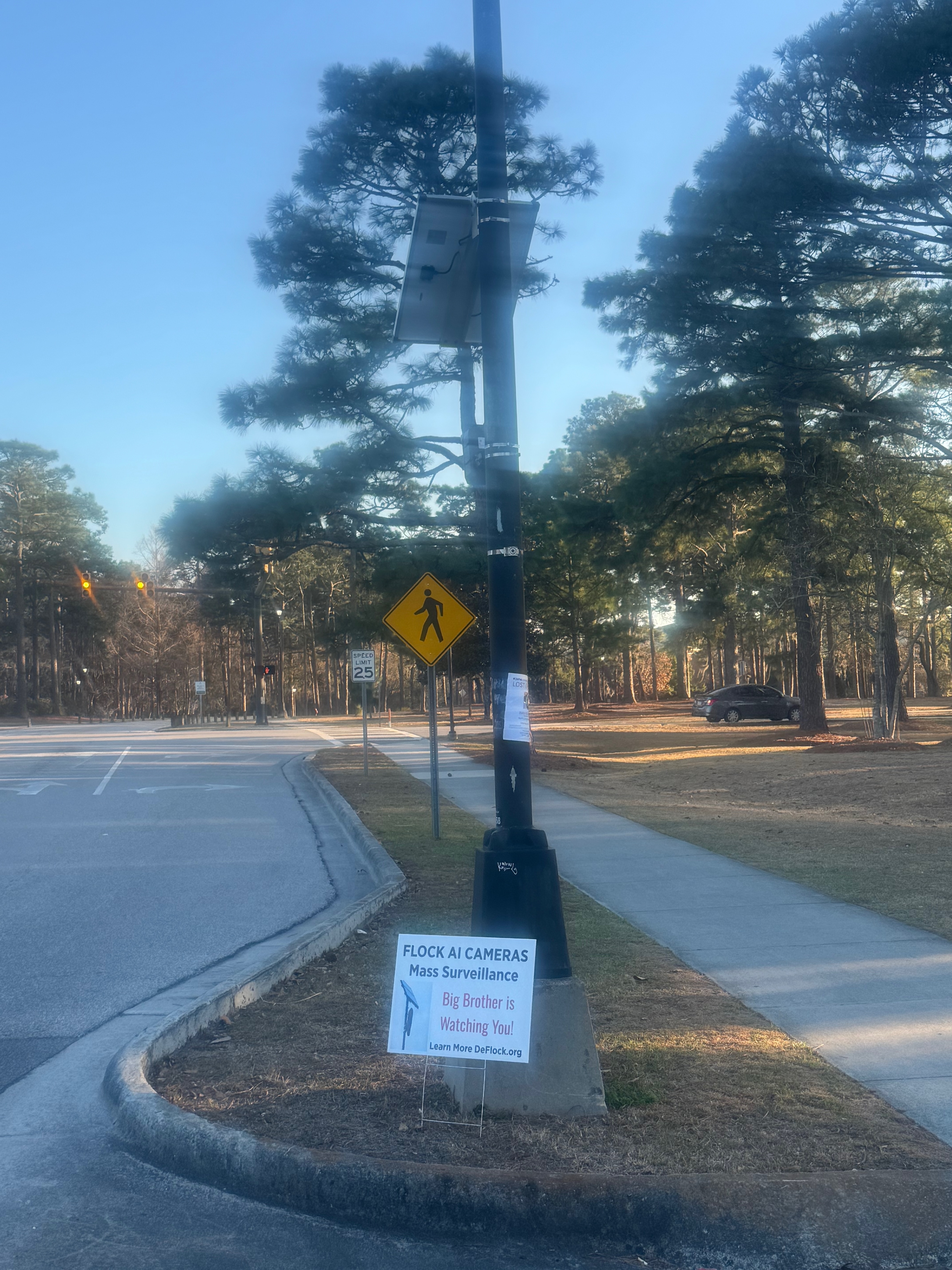 Flock camera on a black pole near UNCW in Wilmington, solar panel on top, at a 25 mph crossing