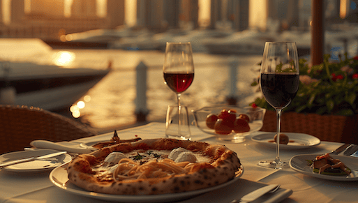 Italienische restaurants in DUbai Italienische restaurants in Dubai - auf einem gedeckten Tisch steht ein Teller mit Pizza und ein Glas mit Wein. Im Hintergrund sind der Hafen und Botte zu sehen.