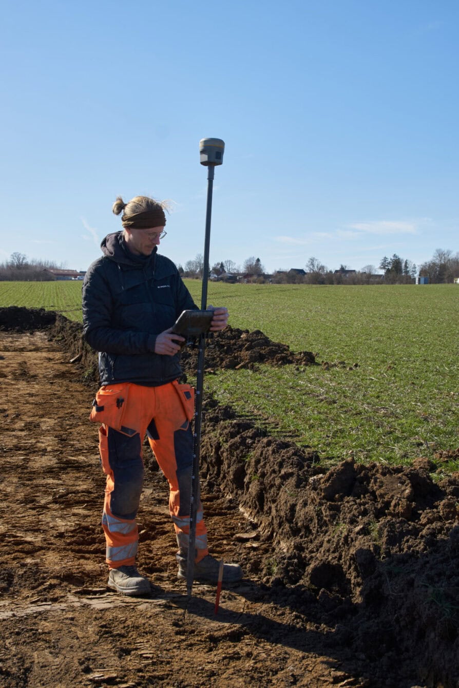 Daniel Teilmann fra Kroppedal Museum er i gang med de arkæologiske undersøgelse af området ved Hedeland forud for Spejdernes lejr 2026. Han opmåler alle registreringer med GPS med få centimeters nøjagtighed, her et lille sort område, der kunne være et gammelt stolpehul. Når leren i et afgrænset områder er mørkere end resten, så har der engang været gravet her, og så skal arkæologerne i gang med skovl og ske for at se om der er noget at finde. 
Foto: Jakob Skipper.
