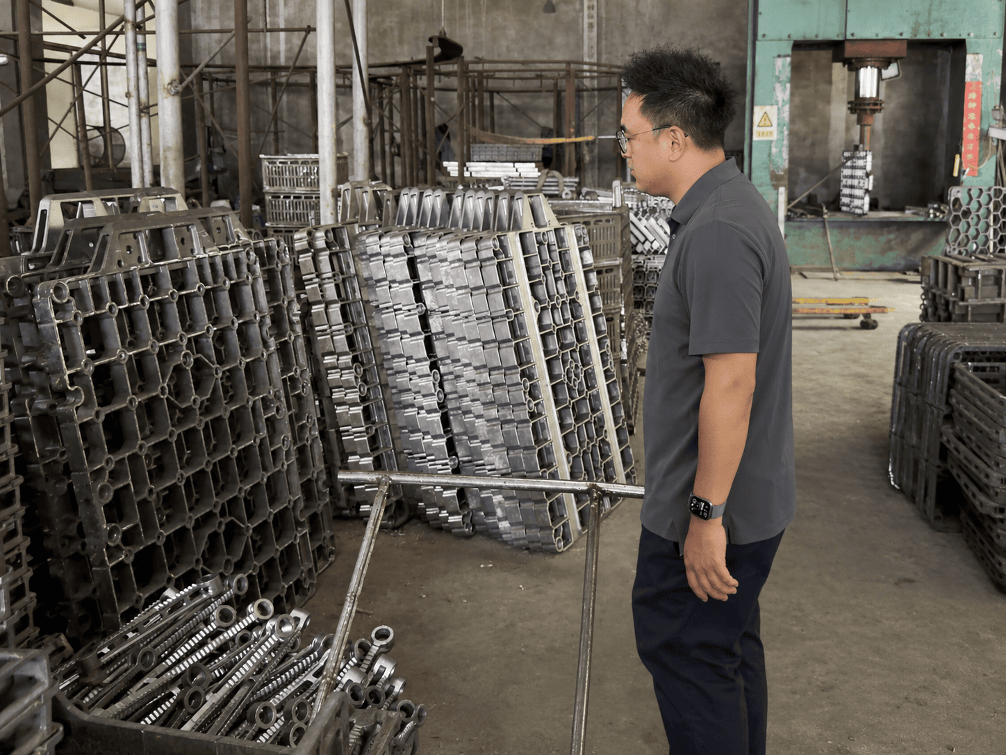Jonny showing stacked open-grid furnace trays and fixture rods in the ECOOSUN workshop