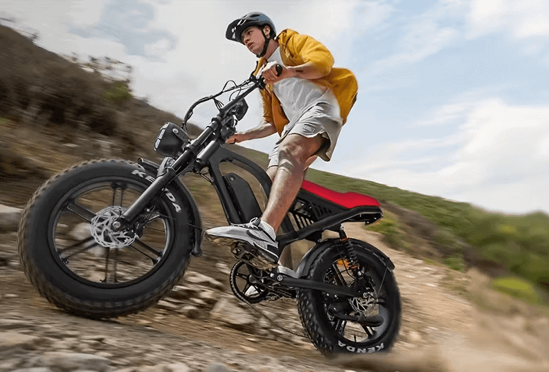 Young man climbing a rocky hillside on a fat-tire electric bike, wearing a helmet and yellow jacket.