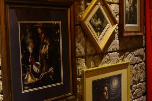 School Of Magic Escape Room | Close up of a wall with paintings with middle painting being crooked and words along the edges