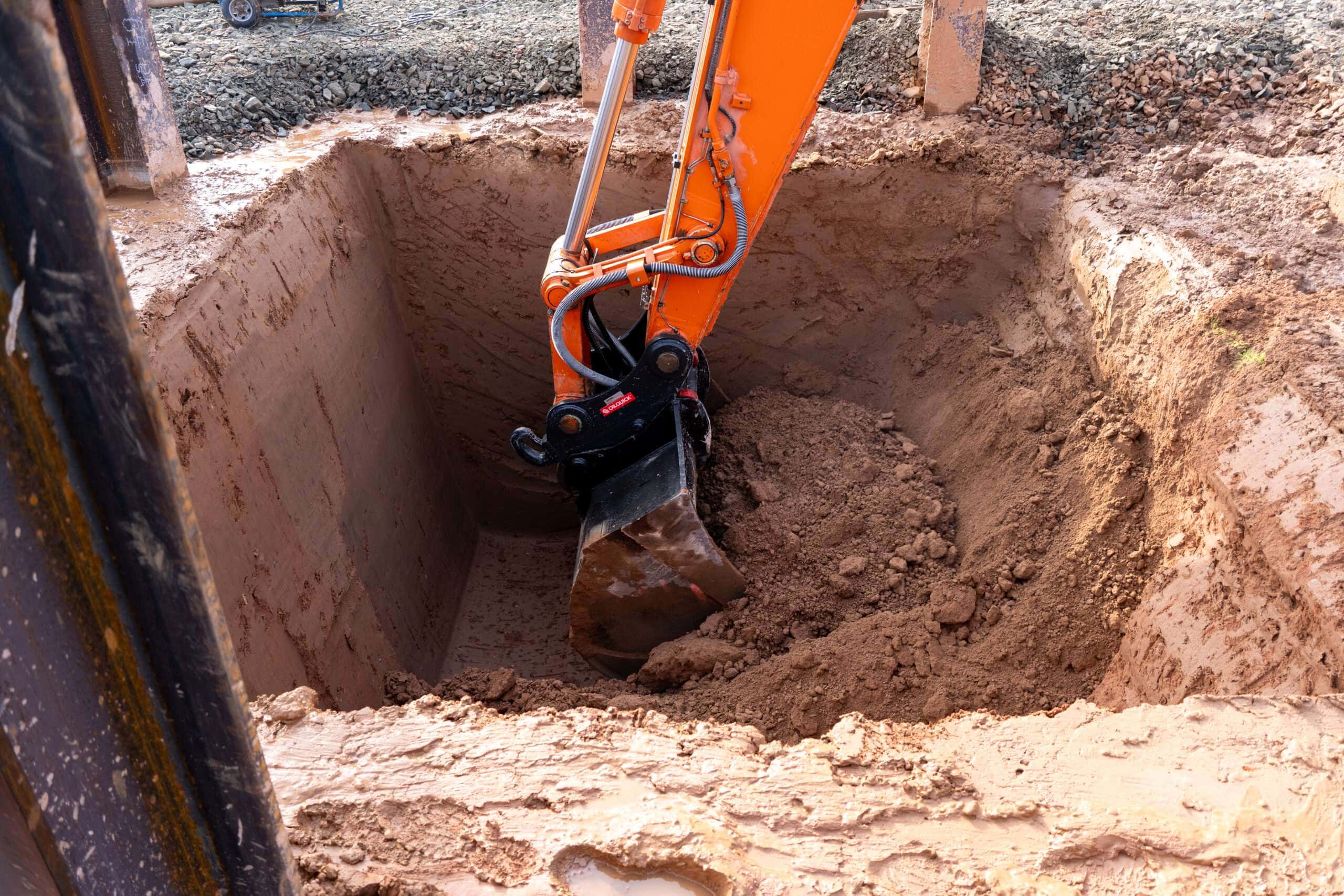 Startgrube, in der eine Baggerschaufel Flüssigboden aushebt.