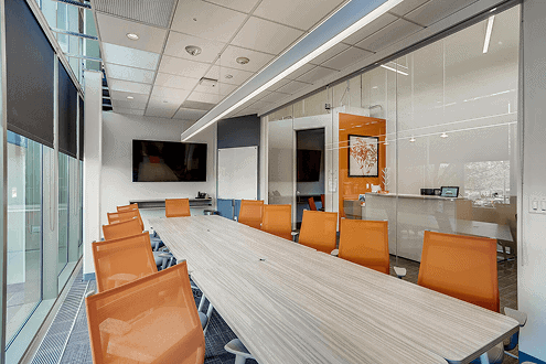 Modern Office Evolution franchising conference room with large table and orange chairs, showcasing professional workspace setup.