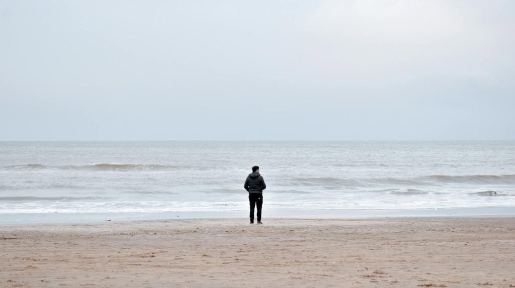 A person stands alone on a beach contemplating