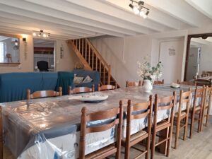 Salle à manger rustique avec table dressée, chaises en bois, canapé bleu et cheminée en pierre
