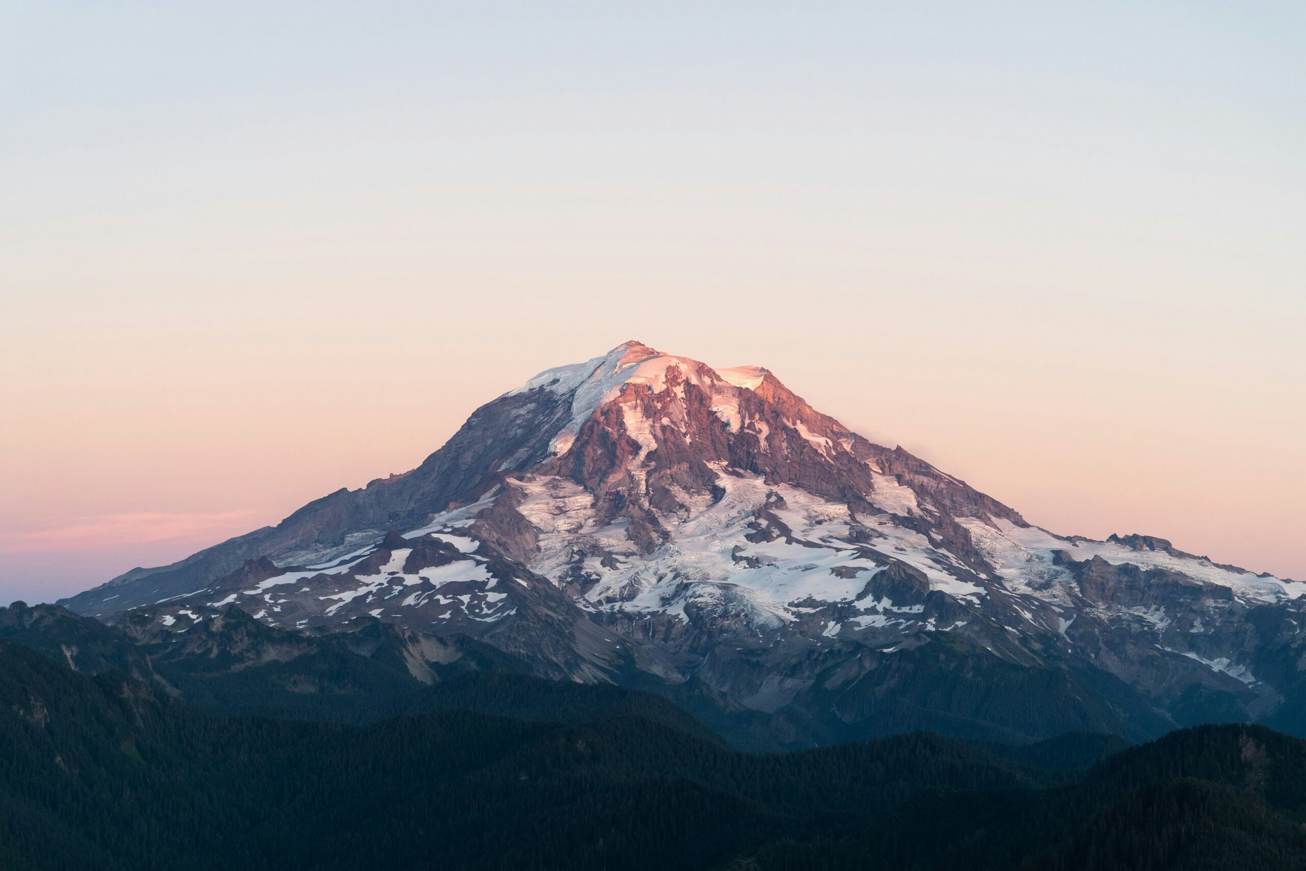 A heavily glaciated Cascade volcano above Pacific Northwest forest, representing Rainier-style mountaineering
