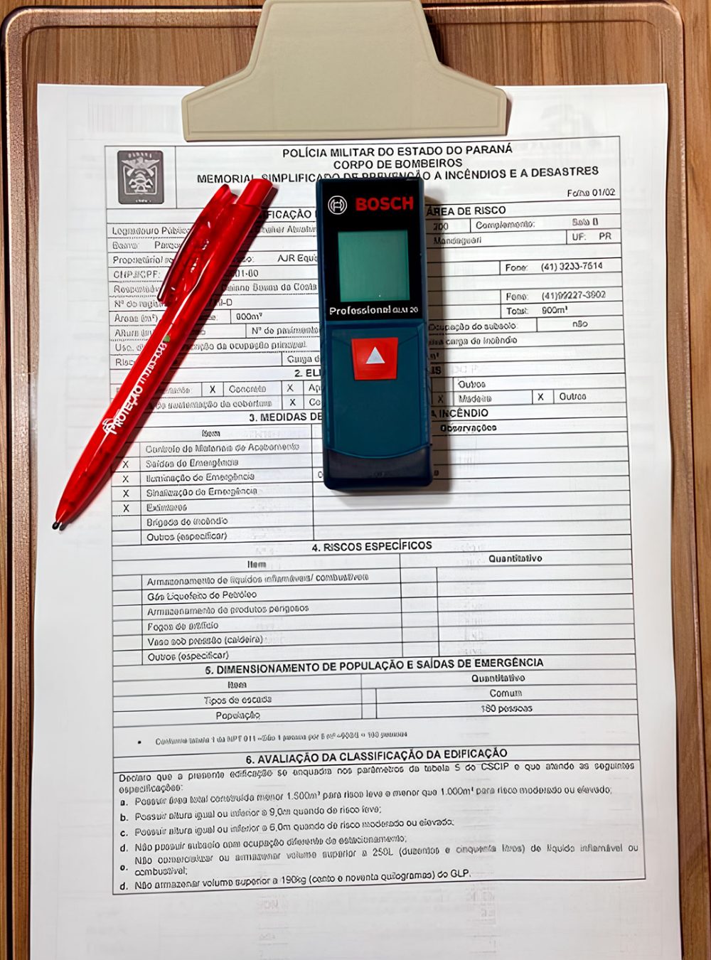 Imagem de um prancheta em uma mesa, com um documento do corpo de bombeiros com uma caneta e um medidor de gás sobre o papel.