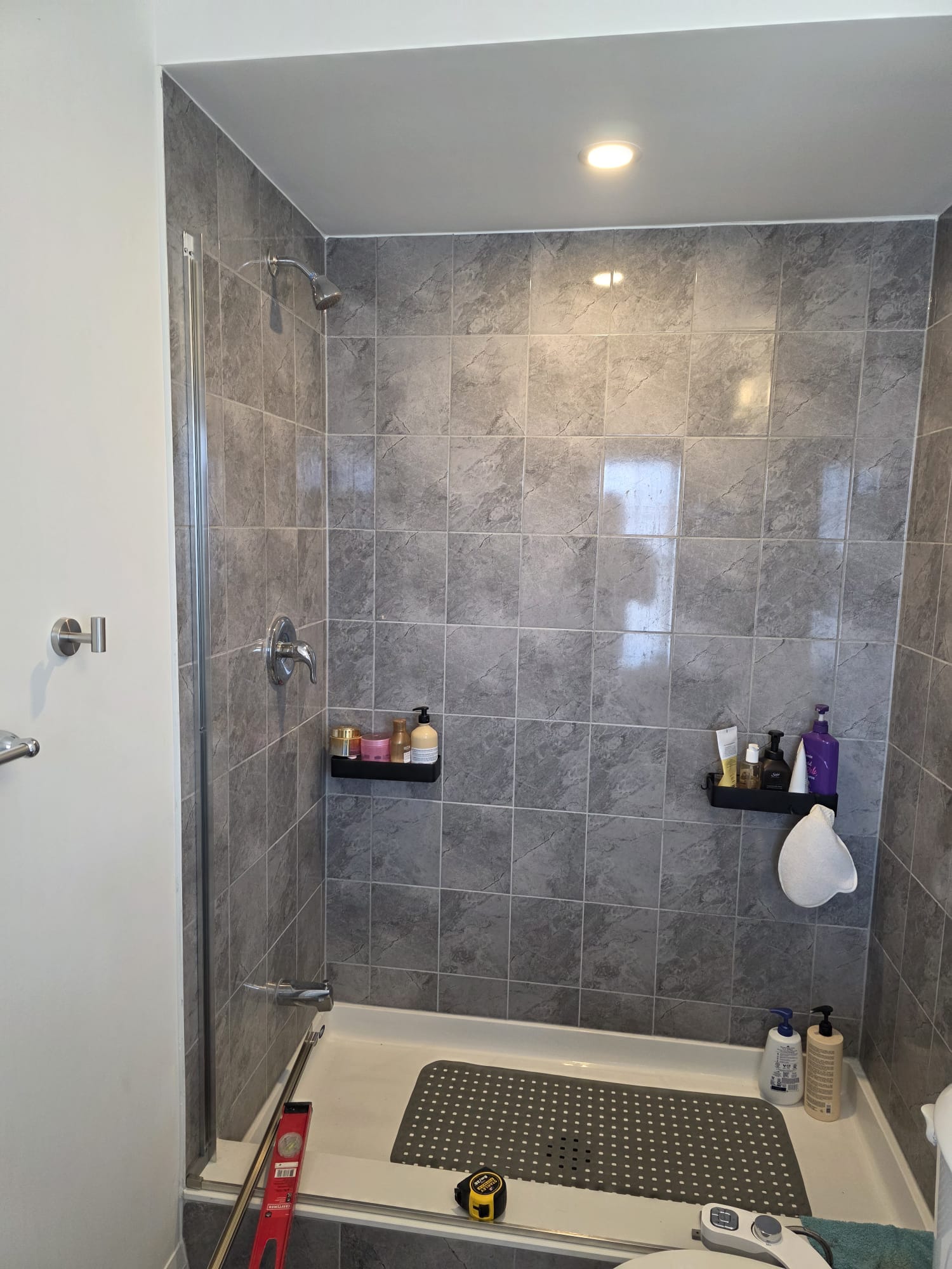 Mid-installation of the custom walk-in shower showing the large-format tile and sliding doors.