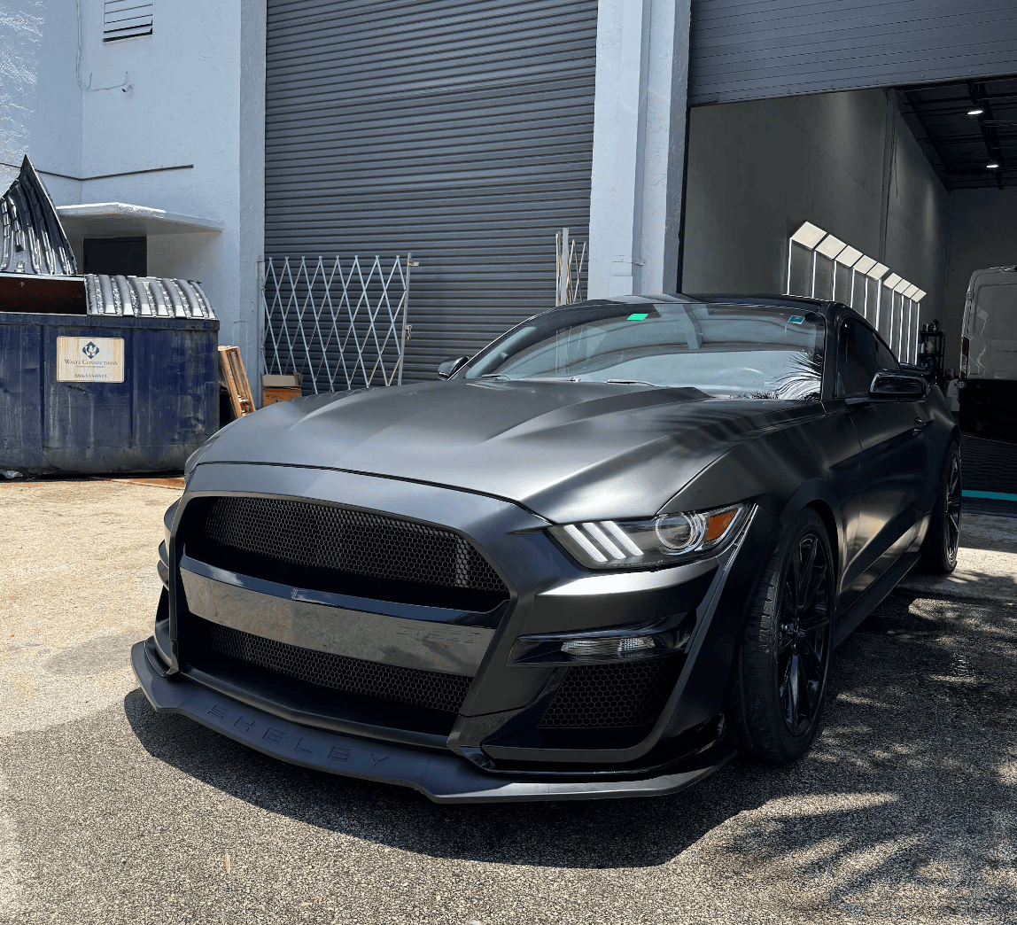 Dark gray sports car parked outside a warehouse with a large roll-up door in the background.