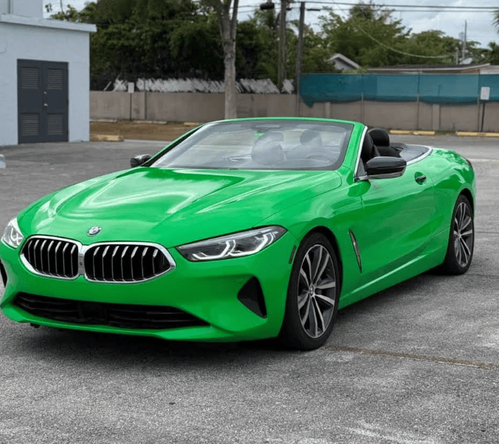 Bright green BMW convertible with the top down, viewed from the front-left, parked on a gray asphalt lot.