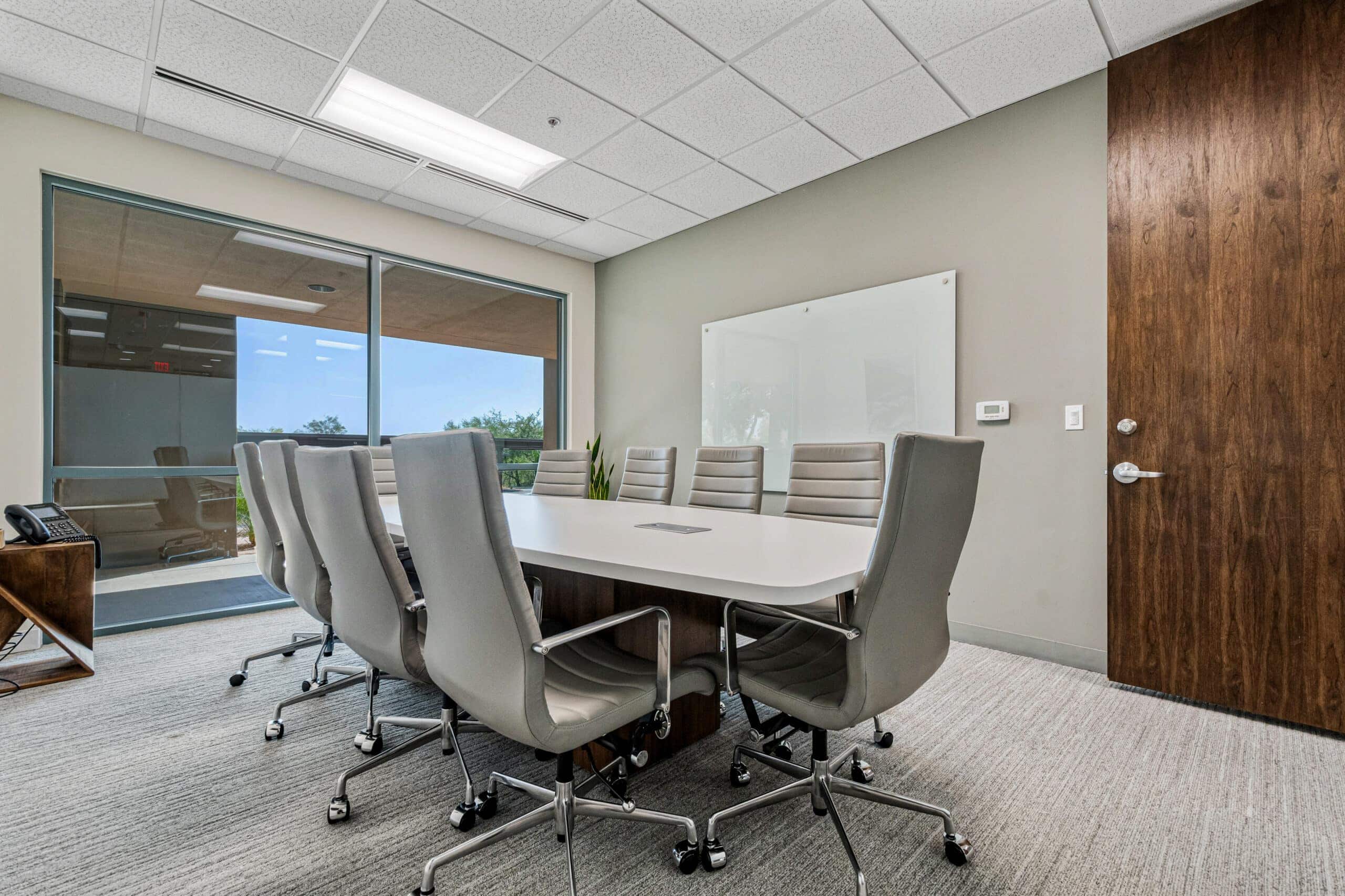 Modern office conference room with white table and gray chairs, large window with city view, ideal for remote and flexible workspaces.