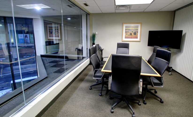 Modern office conference room with glass wall, meeting table, and executive chairs for professional workspace.