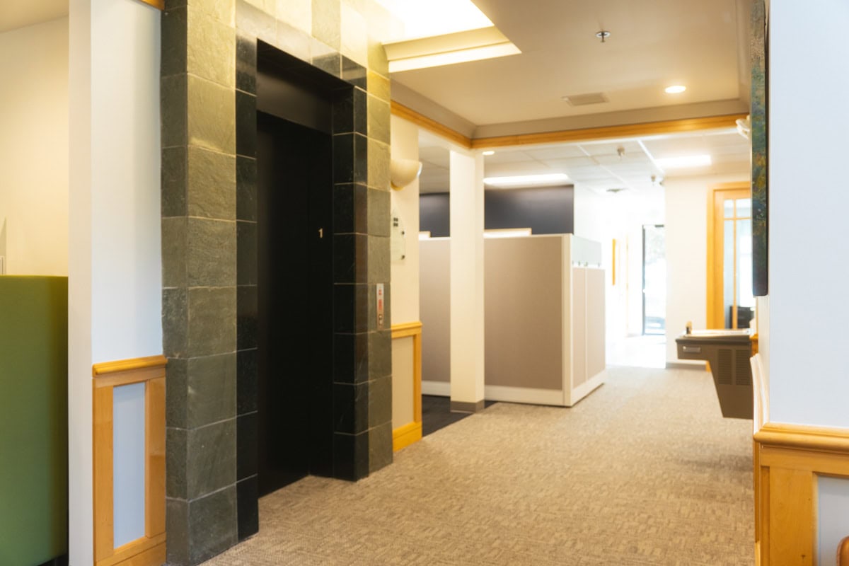 Elevator in a professional office lobby, featuring modern black tile and wood accents, providing convenient access to different floors at Intelligent Office franchise locations.