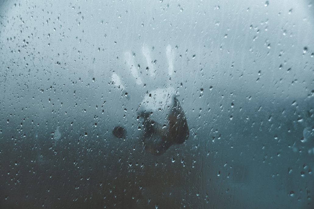 A person's hand is seen pressing against a rainy window, depicting the emotional distress following a job loss.