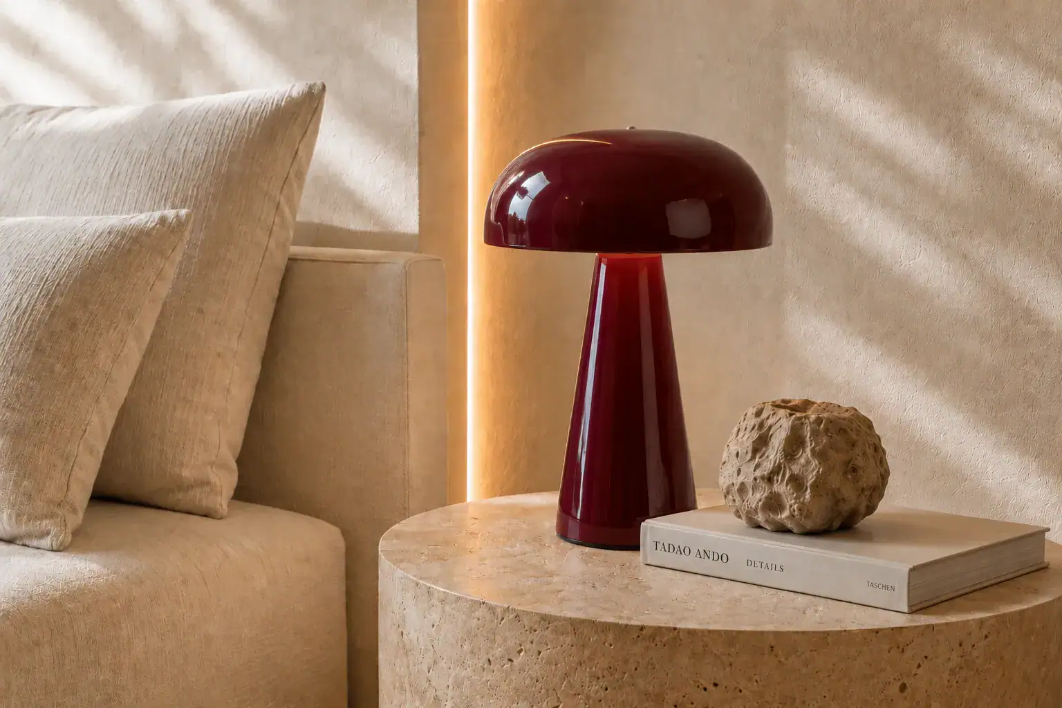 Lámpara de mesa de diseño granate sobre mesa auxiliar de travertino junto a sofá.
