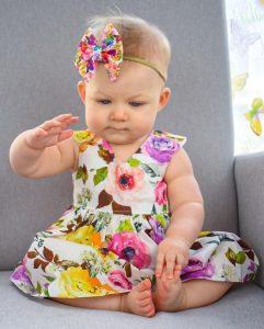 Eloisa Dresses in one of Karousel Kids Handmade Cotton Floral Baby Dresses with a bright Bow headband.