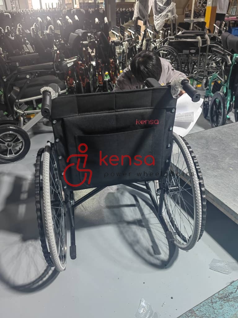 Kensa K-160 siyah manuel tekerlekli sandalye, arkasında Kensa logosu ile üretim hattında sergileniyor.