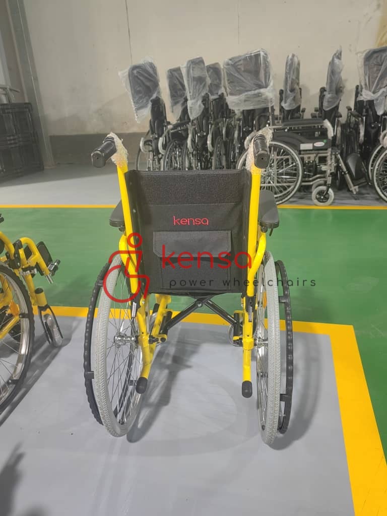 Kensa K-170 16 inç manuel tekerlekli sandalye, sarı metal çerçeveli ve siyah kumaş sırt destekli yapısıyla üretim alanında görüntüleniyor.