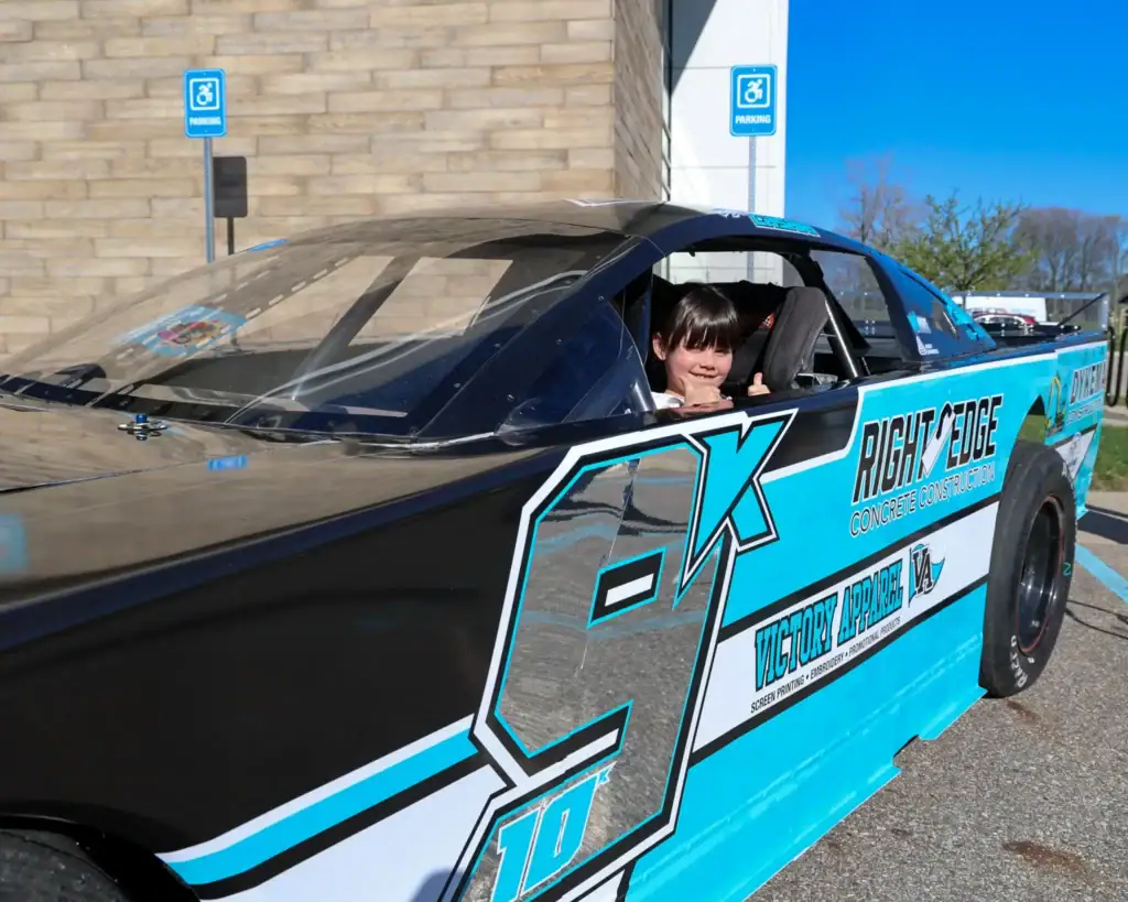 A child smiles from the driver's seat of Adam Casari's race car.