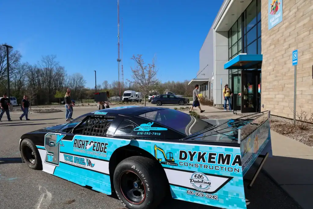 People enter Kids' Food Basket with Adam Casari's race car parked in the foreground.
