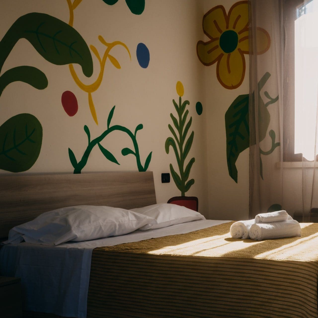 camera hotel con asciugamani sopra al letto e pareti dipinte con fiori