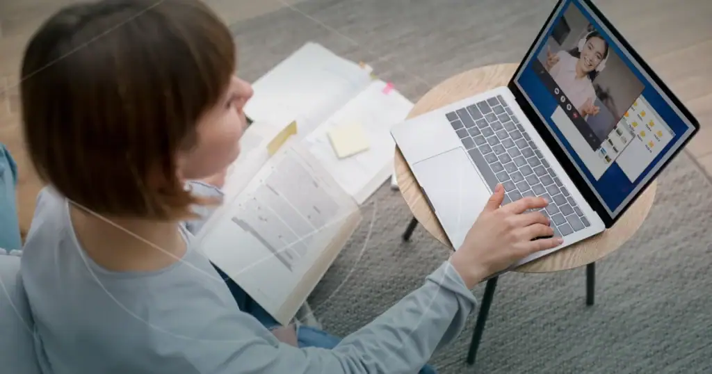 Person, die während einer virtuellen Vorlesung mit einem Tutor auf einem Laptop-Bildschirm Notizen macht