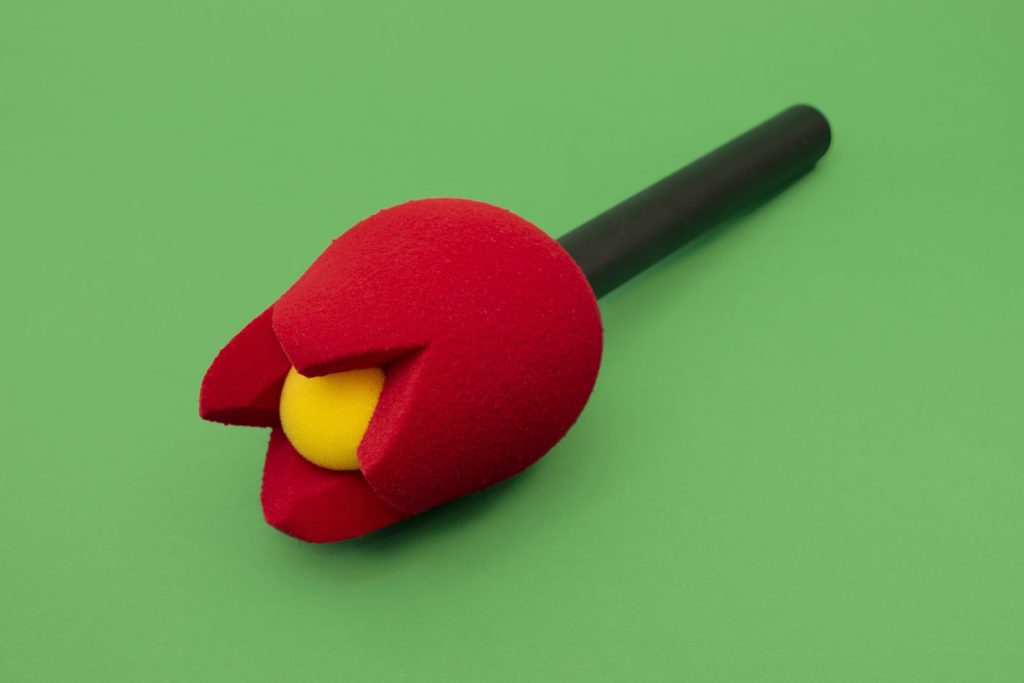 Red flower-shaped foam microphone windscreen with a yellow centre on a handheld microphone, a bespoke 3D acoustic foam cover for broadcast and live production.