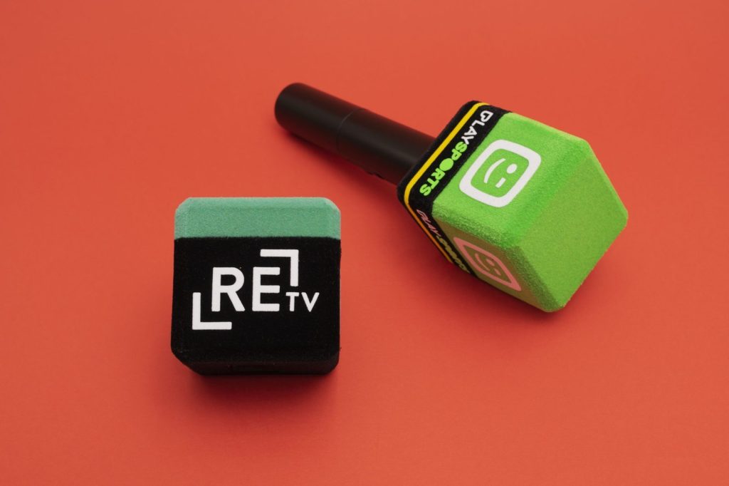 Two 4-sided (square) foam microphone windscreens on a red background: a black and mint-green windscreen with “REtv” branding, and a green square mic flag on a handheld microphone with “PLAY SPORTS” text.