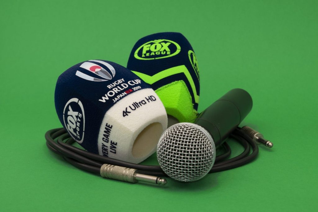 Two 4-sided (square) foam microphone windscreens branded FOX Sports and FOX League, including “Rugby World Cup Japan 2019” and “4K Ultra HD” text, shown with a handheld microphone and cable on a green background.