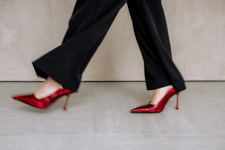 Eine Person, die in einem Haus spazieren geht und dabei eine schwarze Hose und glänzende rote hochhackige Schuhe trägt, wobei nur ihre Beine vor einem hellen Hintergrund zu sehen sind - die perfekte Stilinspiration für jeden Weddingplaner Bayern.