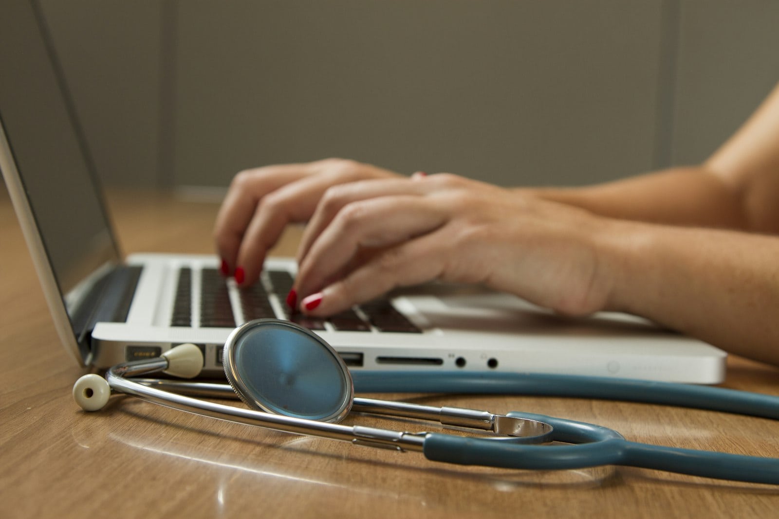 Hands typing on a laptop next to a stethoscope, illustrating searching online platforms like Doctolib to find a doctor in France