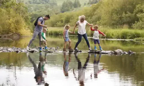 Family Crossing River Whilst Hiking In UK Lake District