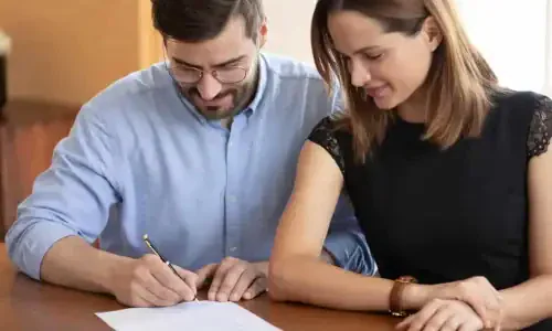 Pleasant young woman watching smiling husband signing contract.