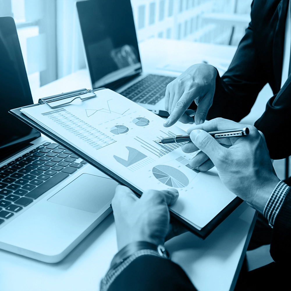 Two employees discussing enterprise risk assessment reports and charts at a meeting desk.