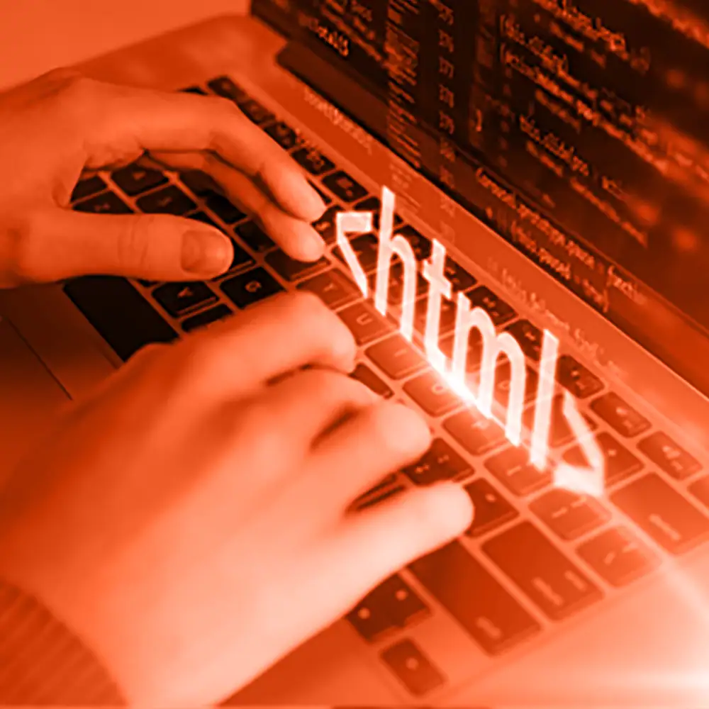 Employee’s hands on a laptop keyboard with “HTML” displayed, representing code review.