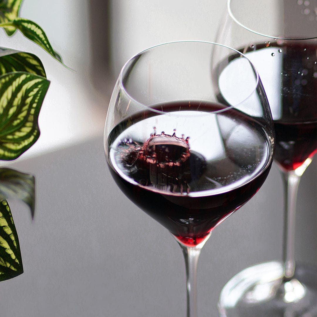 Close-up of red wine splashing in a glass, set against a modern and elegant background at Coco Lounge.