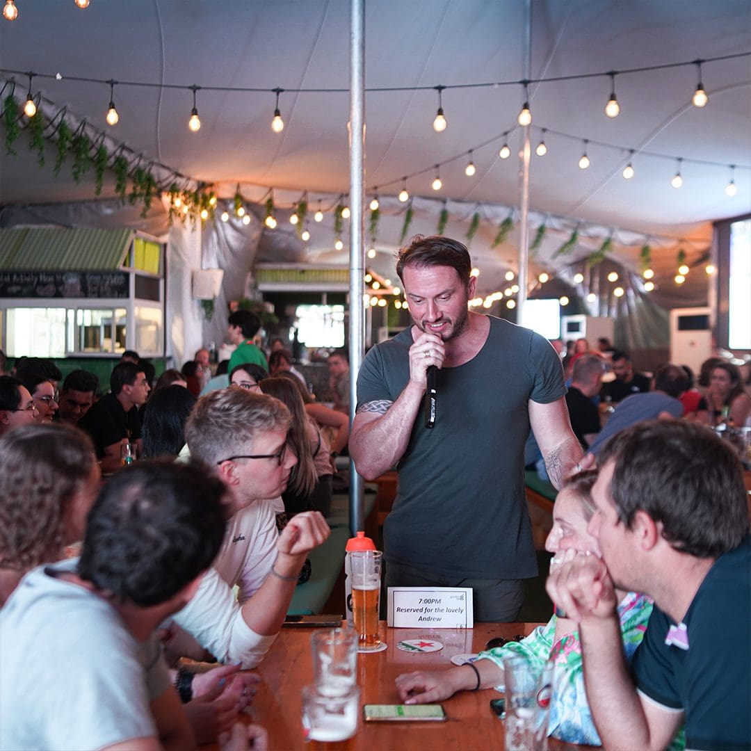 A man speaking into a microphone over a group of people sat at a table.