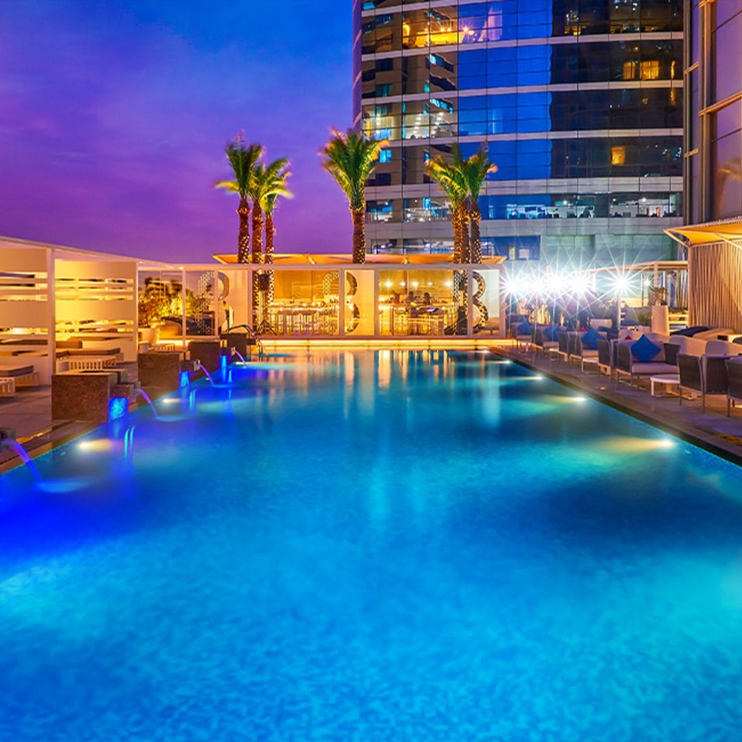 Stunning rooftop pool with palm trees and cityscape reflections at Media One Hotel, perfect for evening relaxation.
