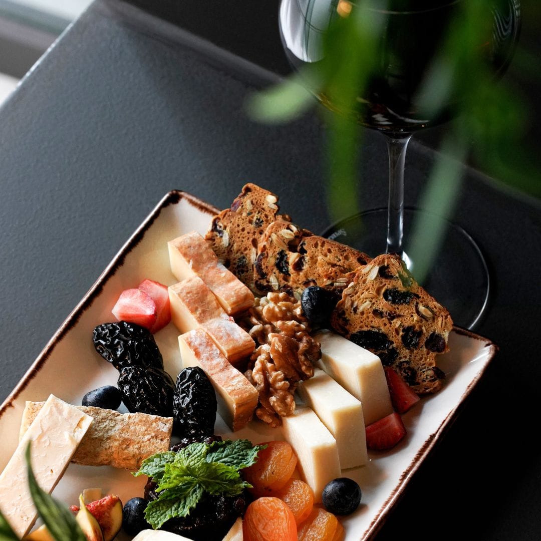 Elegant cheese platter with nuts, dried fruits, and artisanal bread paired with a glass of red wine at Ciao Bella restaurant.