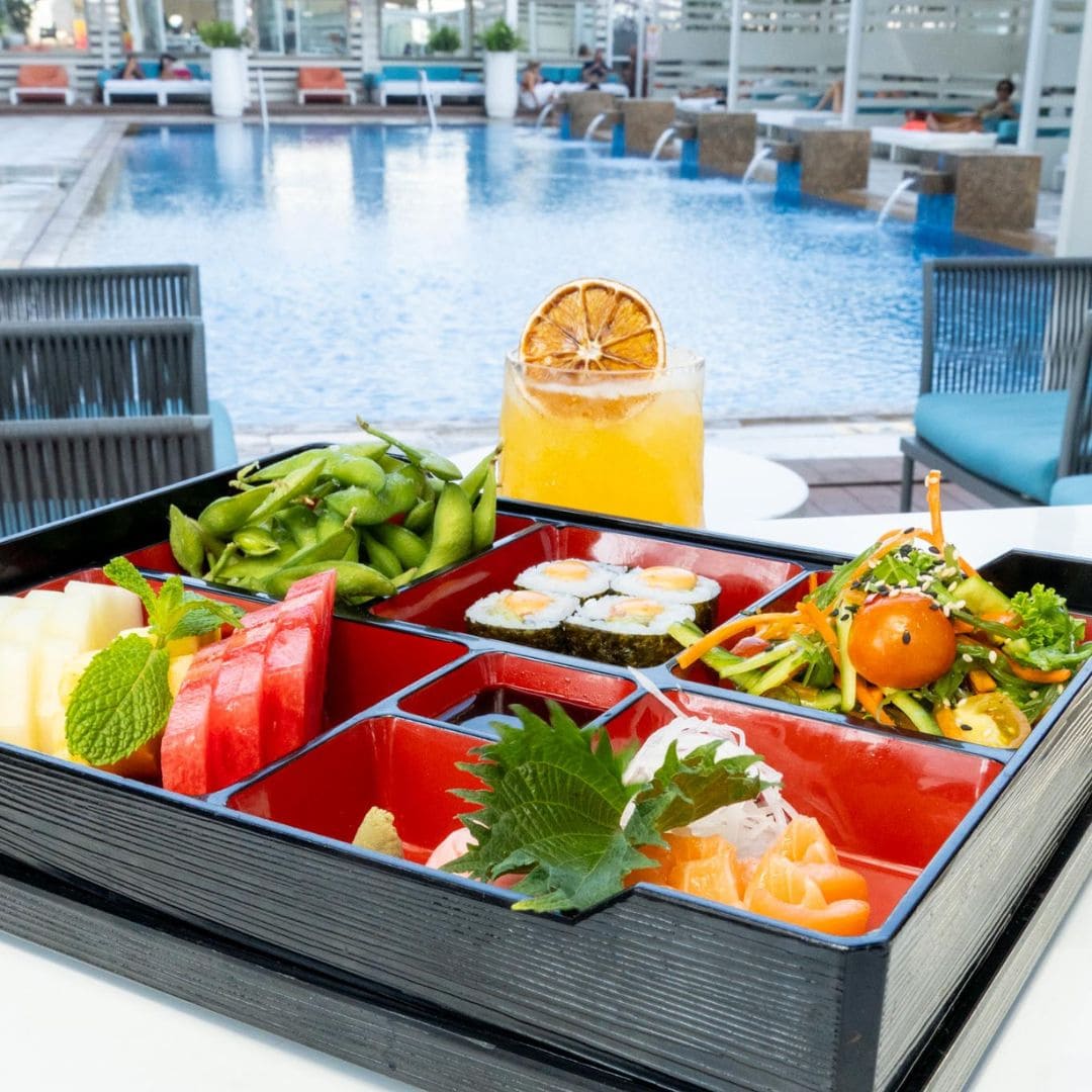 Bento box with sushi, fresh fruit, and edamame served poolside at Coco Lounge, offering a relaxing dining experience.