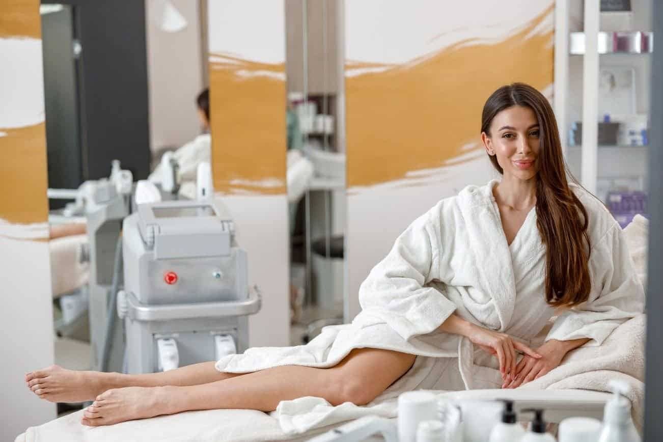 Woman relaxing in a Laser Spa Clinic before laser skin treatments, wearing a white robe next to a laser machine